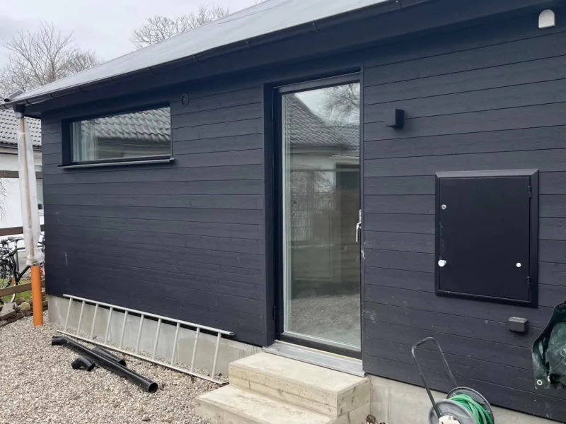 Attefallshus med svart träpanel och glasdörr